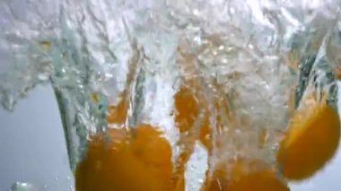 Tam ve dilimlenmiş portakallar suya düşüyor. Besleyici bir meyve. Dilimlenmiş ve tüm portakallar temiz suda beyaz bir zemin üzerinde yüzüyorlar.