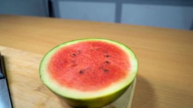 Keskin bir mutfak bıçağıyla yarısı ve dilimlenmiş karpuz. Tahta kesme tahtasının üzerinde saklanmış tohumları olan sulu bir Tarbooj 'un yakından çekimi - tropikal yaz meyvesi 