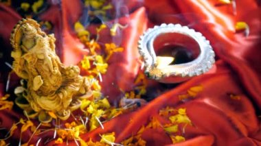 Tütsü çubuğu, Tanrı Ganesha 'nın bir putunun yanına yerleştirilmiş. Hindu ayinleri ve duaları. Petrol lambası / Diya dini bir ibadethanede kadife çiçeği yapraklarıyla kırmızı bir bez üzerinde yanıyor