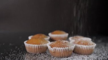 Hintli şefin eli cam masaya pudra şekerli tatlı çörekleri serpiyor. Siyah arkaplandan izole edilmiş kağıt kalıplı nefis ev yapımı kekler. Lezzetli tarif, fırın ve şekerleme, taze pişmiş.