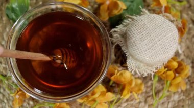 İnsan / dişi bal kasesinin içine tahta kaşık / damlatıcı koyuyor. Paspasın üzerine beyaz bir bez konmuş bir şişe bal. Yemek malzemeleri, organik ürün, yapışkan sıvı, beslenme malzemesi.