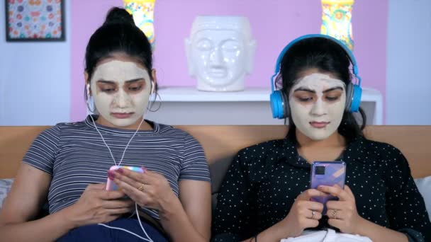 戴面具的好友喜欢在智能手机上听音乐 漂亮的女性 戴着黏土面具 一起在床上放松 健康与美容美发 护肤与治疗 — 图库视频影像
