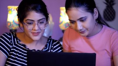 Evdeki yatakta birlikte dizüstü bilgisayar kullanan güzel Hintli kız kardeşler. İnternette sörf yapan gündelik kıyafet giyen en iyi arkadaşlar. İnternet kullanımı, modern yaşam tarzı. Hintli kardeşler.