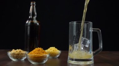 Şeffaf bir kokteyl bardağına dökülen birkaç büyük buz küplü soğuk bira. Lezzetli atıştırmalıklarla servis edilen bir şişe bira. Parti zamanı, kutlamalar, sarhoşluk, keyif.