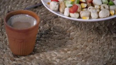 Kadın eli bir tabak Makhana 'yı salatalık, domates ve mısırla tatlandırıyor. Çelik bir kaşıkla bir Kulhad 'da servis edilen sıcak bir fincan çay jüt paspasın üzerinde saklanır - Kulhad Chai, toprağın özü, biyolojik olarak çözülebilir