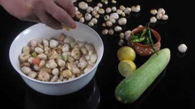 Bir kase Makhana 'ya mısır, domates ve salatalık atan bir kadın. Sağlıklı atıştırmalık. Yarım sulu sarı limon, birkaç yeşil biber ve Pudina yaprakları toprak kabında bir arada tutulur. Hint mutfağı, yemek malzemeleri, kilo kaybı.