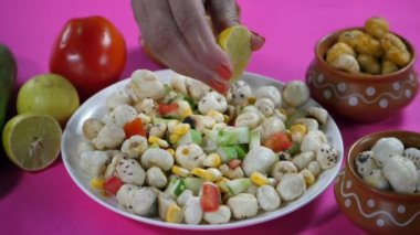 Beyaz seramik tabakta nilüfer tohumlu taze limon suyu sıkan bir kadın. Bir domates, limon ve salatalık ile kızartılmış ve kızartılmış Makhana. Sağlıklı yemek, lezzetli atıştırmalıklar, kilo kaybı, anti-yaşlanma.