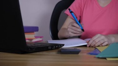 Evde araştırma yaparken dizüstü bilgisayar kullanan pembe tişört giyen genç bir kız. Üniversiteye giden bir öğrenci çevrimiçi derslere katılırken notlar alıyor - video konferansı, uzaktan öğrenme, evden çalışma