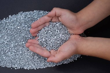 Çocuğun elleri gri arka planda gümüş granülleri tutuyor. Koyu gri arka planda gümüş parçacıkları tutan küçük eller