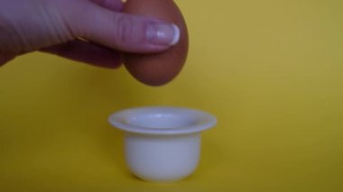 Doğal kahverengi yumurtayı sarı arka planda basit bir beyaz yumurta kabına yerleştirir. Kahvaltılık yemek. Minimalist doğal Paskalya teması.