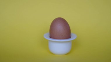 El, sarı arka plandaki basit beyaz yumurta yumurtasından doğal kahverengi yumurtayı alır. Kahvaltılık yemek. Minimalist doğal Paskalya teması.