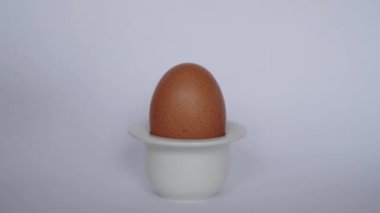 El, beyaz arka plandaki basit beyaz yumurta yumurtasından doğal kahverengi yumurtayı alır. Kahvaltılık yemek. Minimalist doğal Paskalya teması.