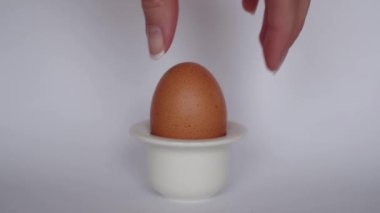 El, beyaz arka plandaki basit beyaz yumurta yumurtasından doğal kahverengi yumurtayı alır. Kahvaltılık yemek. Minimalist doğal Paskalya teması.