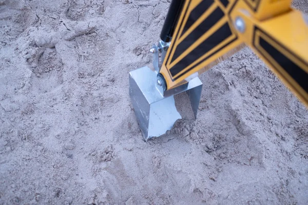Hydraulically controlled arms of a yellow digger. Playful mini kids excavator in a sand pit.
