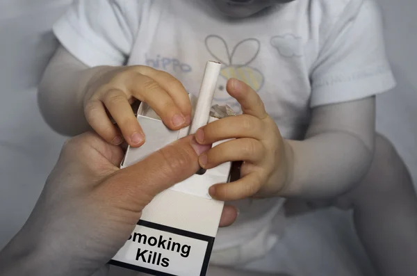 Adulto dando cigarrillos a un bebé pequeño. Fumar mata. Lo es. — Foto de Stock