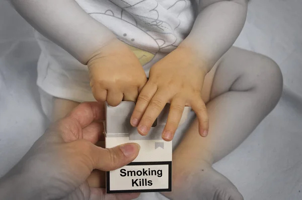 Adulto dando cigarrillos a un bebé pequeño. Fumar mata. Lo es. —  Fotos de Stock