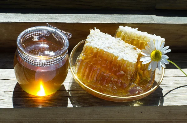 Favos de mel e mel em um frasco de vidro em uma soleira da janela de madeira em um — Fotografia de Stock