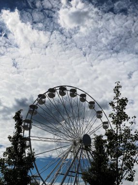 Bulutlu gökyüzünün arka planında kabinleri olan bir dönme dolap görüntüsü