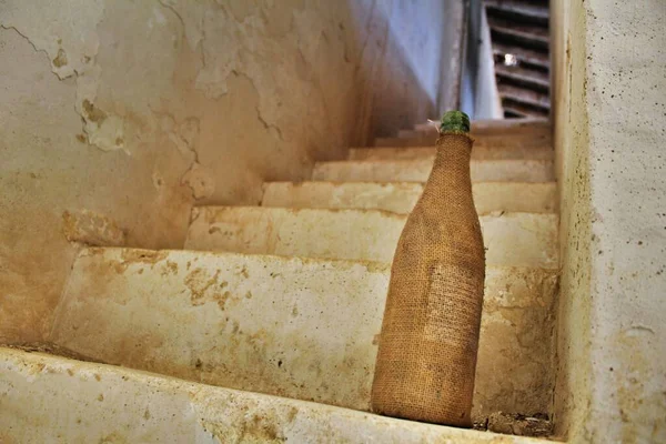 Eski bir evdeki eski bir merdivenin üzerinde bez kaplı eski boş şarap şişesi.