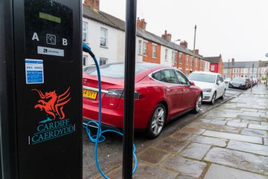 Cardiff, Wales, İngiltere - 14 Şubat 2021: Kırmızı Tesla, elektrikli araba (EV), Cardiff Konseyi tarafından sağlanan bir iskan caddesinde şarj noktası kullanıyor