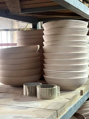 Clay, bir çömlek atölyesinde şekil değiştiriyor. Tabaklar ve kaseler ahşap raflarda düzgünce diziliyor..