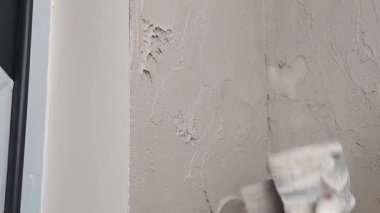 Oturma odasındaki bir geliştirme projesi sırasında duvarlara alçı yapıştırırken görülüyor. Süreç, yenilenmek üzere yüzeyi düzleştirmeyi ve tamamlamayı içeriyor.