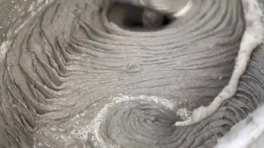 Gri çimentoyu karıştırma işlemi dönen bir mikserde maddelerin harmanlandığını gösteriyor. Bu, sonraki inşaat faaliyetleri için önemli bir adımdır..