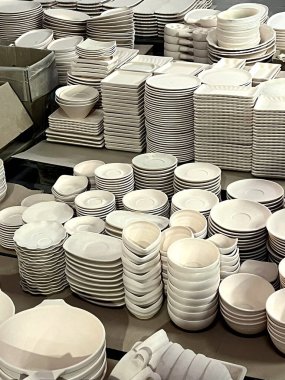 Cilalanmamış seramik tabaklar ve kaseler dikkatle bir atölyede düzenlenir, kil fırlatmaya hazırlanma sürecini gözler önüne serer.