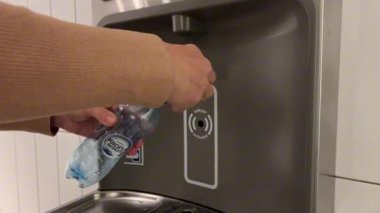 Kanada mı? Ontario - 10.17.23 Bir kişi halka açık bir alanda bulunan bir su dağıtıcısına plastik bir su şişesi dolduruyor. Süreç, suyun şişeye aktığını gösteriyor..