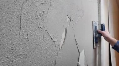 Bir insan duvarda eski alçıyı kazıyarak ve üzerine yeni alçı yapıştırarak çalışır. Etkinlik gündüz vakti bir inşaat alanında gerçekleşiyor..