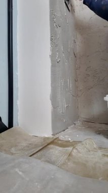 Bir adam, inşaat alanında alçılı bir duvarı malayla düzleştiriyor. Düz bir zemin oluşturmak için köşelerde ve kenarlarda çalışır..