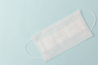 Mavi arka planda beyaz tıbbi maske var. Kirliliğe, virüse, gribe ve koronavirüse karşı yüz maskesi koruması. Sağlık ve Cerrahi Konsept.
