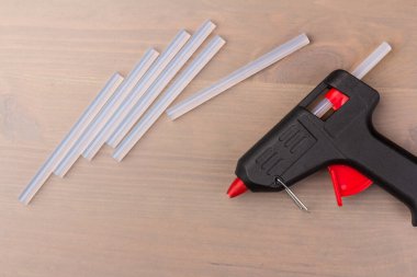 Sıcak eritilmiş silah, inşaat aletleri. Ahşap arka planda tutkal tabancası ve çubuklar.