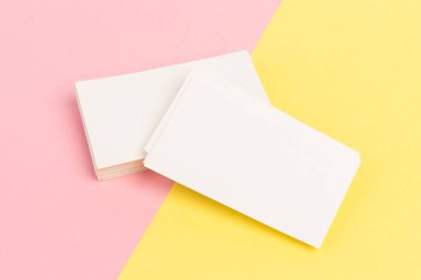 Pembe ve sarı arkaplanda yakın planda beyaz, boş kartvizitler.