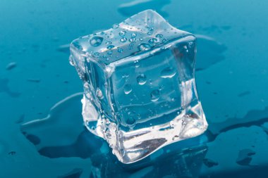 Bir tane eritilmiş buz küpü. Buz küpleri ve su damlaları mavi arkaplanı kapatır