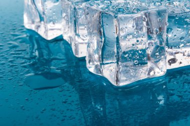 Erimiş buz küplerinin piramidi damlalarla. Buz küpleri ve su mavi arkaplana düşer.