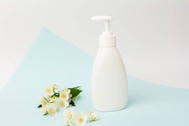 Cilt bakımı kozmetik ürünleri, vücut losyonu, çamaşır jeli ya da mavi arka planda yasemin çiçekleri olan pompalı beyaz şişedeki sıvı sabun.