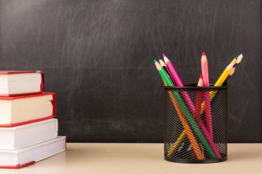 Tel örgü bardaktaki renkli kalemler, tahta masadaki kara tahta zemin, eğitim veya okula dönüş konsepti olan kitaplar.