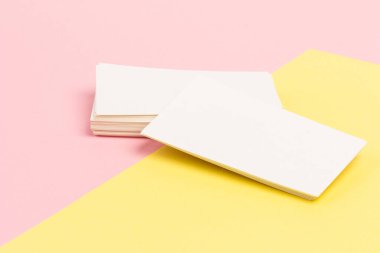 Pembe ve sarı arkaplanda yakın planda beyaz, boş kartvizitler.