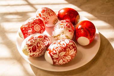 Beyaz bir tabakta bej bir masada kırmızı ve beyaz Paskalya yumurtaları süslenmiş. Gölge çizimi. Paskalya Konsepti.