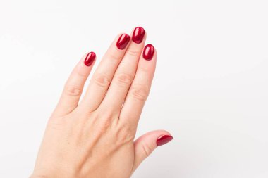 Beyaz arka planda tırnaklarında koyu kırmızı manikür olan genç bir kadının ellerine yakın çekim.