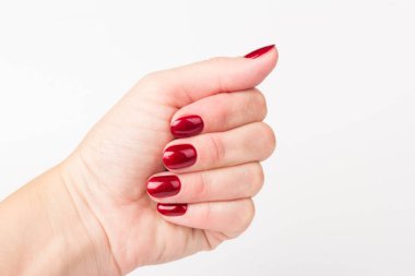 Beyaz arka planda tırnaklarında koyu kırmızı manikür olan genç bir kadının ellerine yakın çekim.