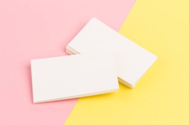 Pembe ve sarı arkaplanda yakın planda beyaz, boş kartvizitler.