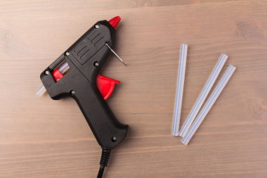 Sıcak eritilmiş silah, inşaat aletleri. Ahşap arka planda tutkal tabancası ve çubuklar.