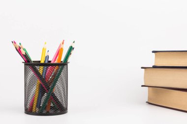 Tel örgü bardaktaki renkli kalemler, beyaz arkaplan, eğitim veya okula dönüş konsepti üzerine kitaplar.