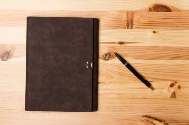 Tahta arka planda duran siyah bir kalem ve defter ile üst görünüm modelleme şablonu.