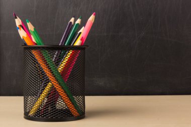 Siyah tutacağa renkli kalemler. Okul ve ofis malzemeleri karatahtanın önündeki sınıf masasında. Kopyalama alanı ile göster