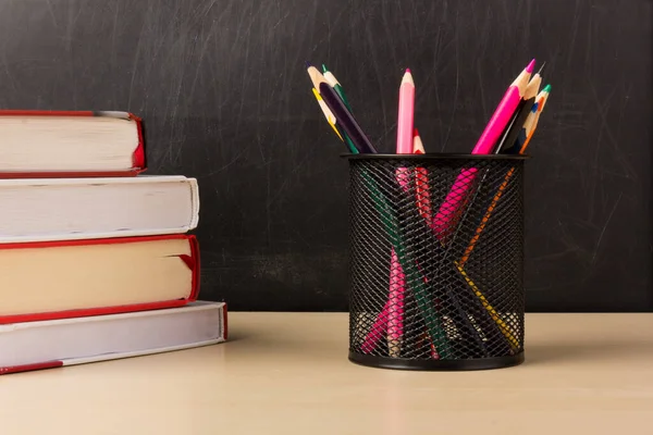 Colorful pencils in wire mesh cup,books on wood table with chalkboard back ground, education or back to school concept