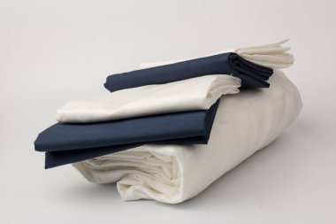 Beyaz üzerine katlanmış beyaz ve mavi yatak çarşafları ve yastık kılıfları yığını; arkaplan; kapanış.