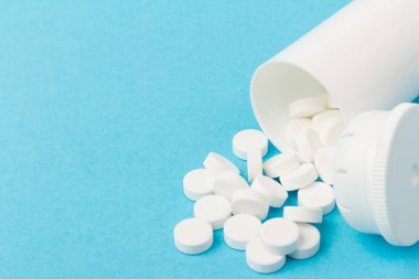 İlaç şişesi ve beyaz haplar mavi renkli arka plana dökülmüş. İlaç ve reçeteli haplar.